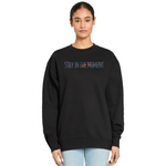 Black sweatshirt with 'Stay in the Moment' text worn by a person on a white background