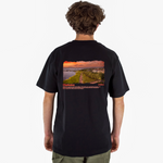 Person wearing a black t-shirt with a scenic print on the back, standing against a white background