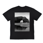 Black t-shirt with a scenic print of a rock arch over water on a white background