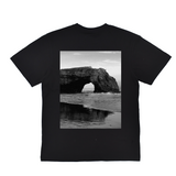 Black t-shirt with a scenic print of a rock arch over water on a white background